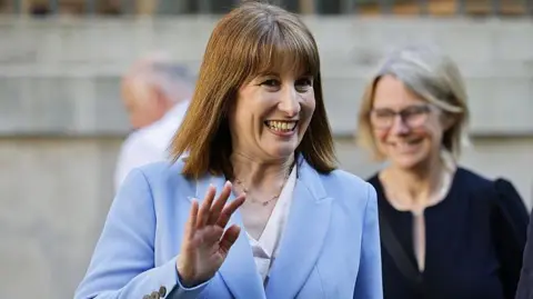 Rachel Reeves, chancellor of the UK, smiling and waving. She is wearing a light blue suit.