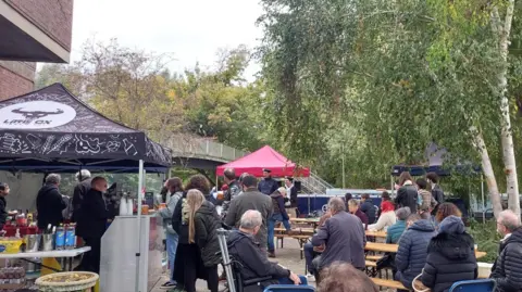 BBC A crowd of people at Mount Place during Jericho's Oktoberfest on 17 October. Some are buying food and drinks while others are watching a band perform. A tent branded Little Ox Brew can be seen. It is cloudy.
