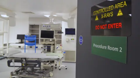 View through an open door - which carries a warning about x-rays - to a hospital room with a specialist bed and a number of computer monitors