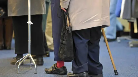 A general view of elderly people. There is a walking stick and a walking frame. 