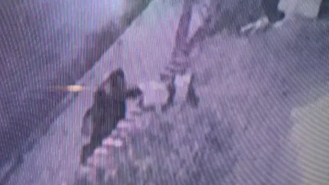 Other Blurry CCTV footage shows a person with their hand in a box on a wall at the front of a house by a road