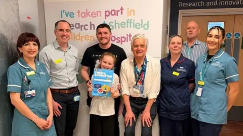 FAMILY HANDOUT A child, Ellie, with a group of hospital staff and her dad, they smile for a photograph