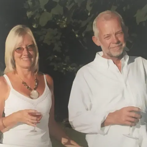 Family handout Margaret Manion wears a white top and stands with her partner against a green background, in sunshine