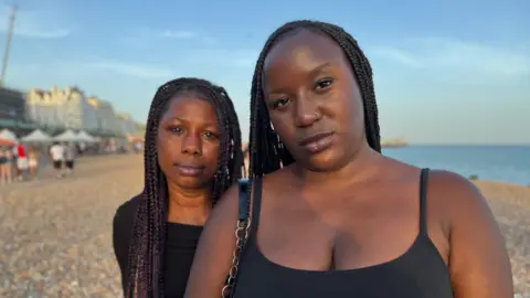 Charlie Rose / BBC Two women wearing black tops. They are stood next to each other on a stony beach, with the sea in the background.