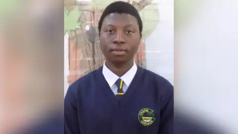 Matt is looking at the camera, it is a school photo. He is wearing a navy blue school jumper and shirt and tie underneath.