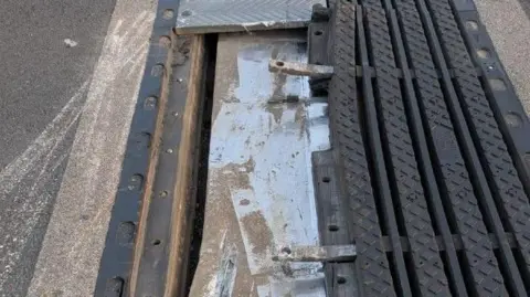 A close-up photo of a damaged metal joint along a motorway. The metal of the joint has been taken away and several parts are sticking out.