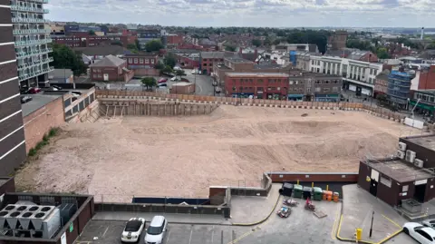 An elevated view showing the site of the former department stores having been demolished. The vast site is boarded off around its perimiter.