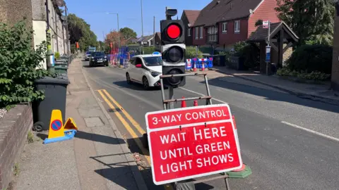 Main Road in Sutton-at-Hone with temporary traffic lights and roadworks causing one lane to be closed to traffic