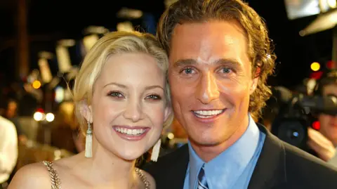 Kate Hudson and Matthew McConaughey standing together and smiling in formal dress, with red carpet activity behind them