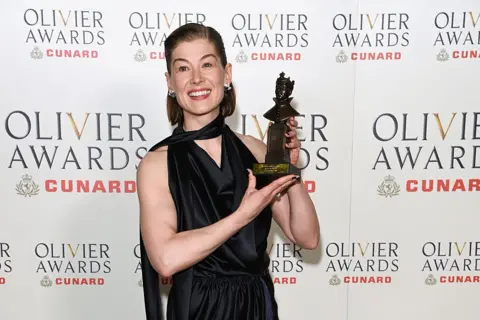 Getty Images Rosamund Pike in a black dress holding an Olivier award