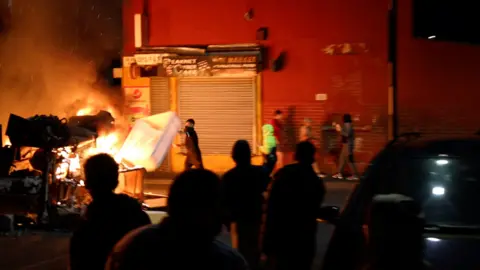 A man throws an item onto a fire during unrest in Harehills.