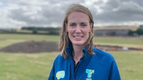 A woman with shoulder-length brown hair, wearing a blue jacket, looks at the camera