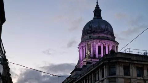 Ground level view of Nottingham's Council House dome, lit purple against an evening sky