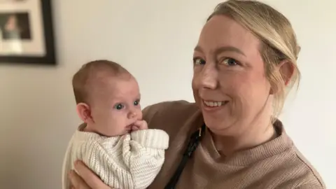 Melissa Hawksley looking at the camera while holding baby Millie 