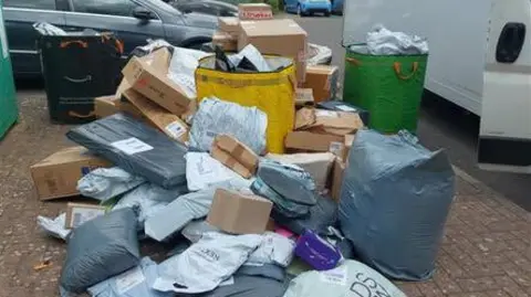 Large bags, cardboard boxes and small plastic bags all piled on the ground next to a white van.