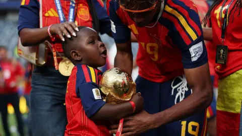 Fifa/Getty Images Kenye holds the World Cup trophy supported by his older brother
