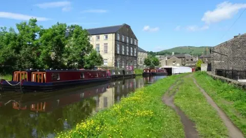 The Leeds and Liverpool Canal at Silsden, with narrow boats moored on the far side.