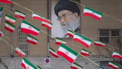 NurPhoto via Getty Images A mural of Iran's Supreme Leader Ayatollah Ali Khamenei is seen on the side of a building in Azadi avenue with reams of Iranian national flags hanging in the foreground, in Tehran on 11 February 2022.