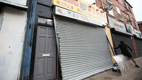  REX/Shutterstock Broken shutter on a tobbaco and vape shop which was ransacked