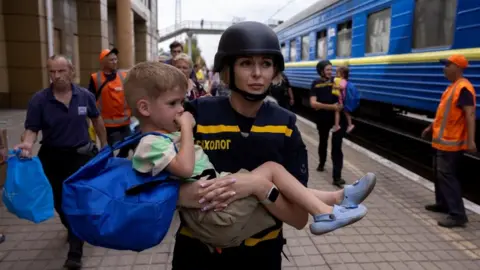 REUTERS/Thomas Peter An emergency service worker carries a child as local residents flee on an evacuation train from Russian troop advances in Pokrovsk, Ukraine, amid Russia's attack on Ukraine, August 22, 2024