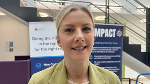 Caroline McGlade is wearing a light green jacket and smiling in front of two Cleveland Police posters in the background.