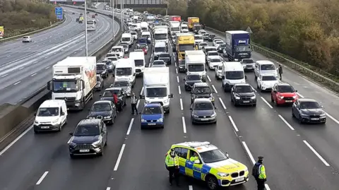 PA Media / Just Stop Oil A police car blocks six lanes of traffic across the M25 