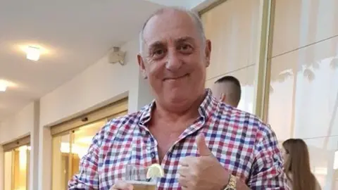 Bill Sheargold A man in a checked shirt smiling with his thumb up while holding a drink with a lemon slice