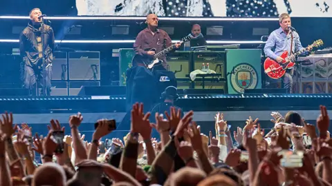 Fans wave their hands above their heads as Oasis perform on stage
