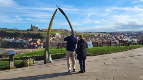 LDRS A man and a woman are stood in front of the Whale Bone Arch. 