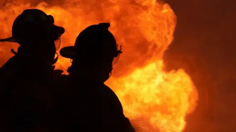 Getty Two silhouettes of firefighters in full uniform tackle a large blaze.