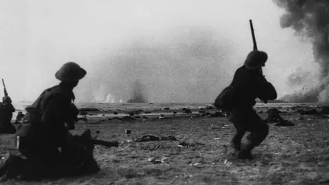 Getty Images Two British soldiers from World War Two fight with explosions in the distance.