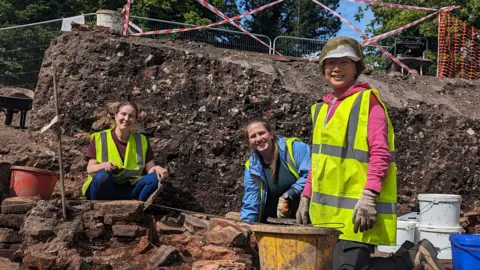 Anna Giecco Three women smiling to the camera in the middle of an archaeological dig
