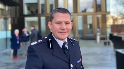 Laura Coffey/BBC A man in full police uniform outside an office building. He has short grey hair.