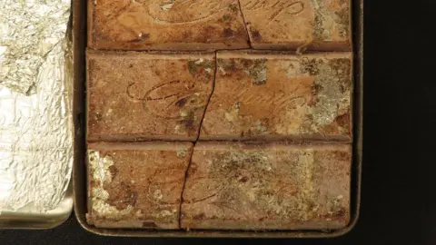 Lockdales Auctioneers and Valuers A close up view of a chocolate bar from 1900. The word Cadbury is on the chocolate. The is a large crack through the middle of the bar. 