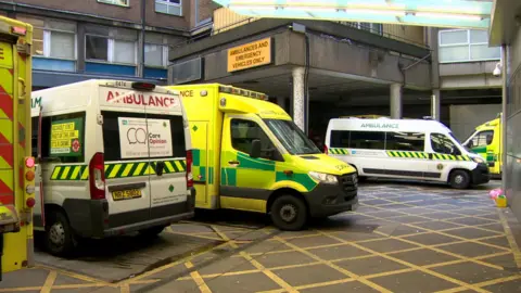 BBC The exterior of the ambulance bay of the Royal Victoria Hospital in Belfast. There are multiple ambulances parked outside the brown exterior door.