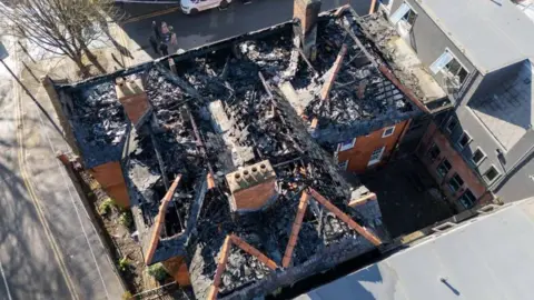 Aerial view of the roof showing significant damage with chimneys standing but most of roof burnt down.