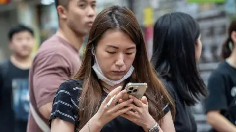 A woman holding a cigarette and looking at her phone in Hong Kong, China, on June 6, 2024