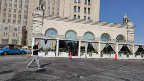 EPA Man walking past the restaurant where the explosion happened, the glass windows are behind metal fencing. 