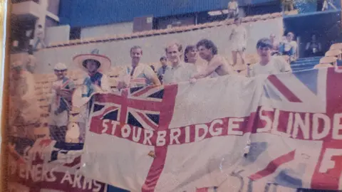Gary Allen A faded photograph of fans in a football stadium holding an England fan which says 'Stourbridge' on it.