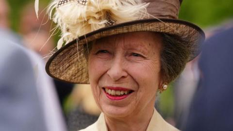 Princess Anne in a yellow hat with feathers on it. 