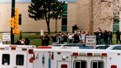 Getty Images is granted more than ten armed accompanying students from Columbin Secondary School in Colorado, USA, after two teenagers went on the fire. The students, who were depicted from a distance in a straight line and their hands are traveling on their heads. Two white "Right Lane Must Turn Right" The signs are clear and that the linear ambulance is parked.