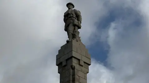 A statue depicting an infantry soldier on top of the Douglas war memorial, which made of grey stone.