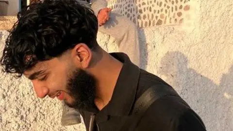 Just Giving Man with dark hair and beard, young, in black polo top in sunshine.