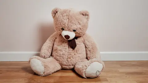 Getty Images A lone teddy bear sits on a brown wooden floor