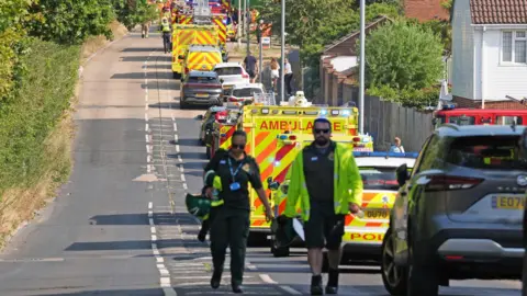 PA Media A long line of ambulances and police cars parked on a road parallel to the railway line