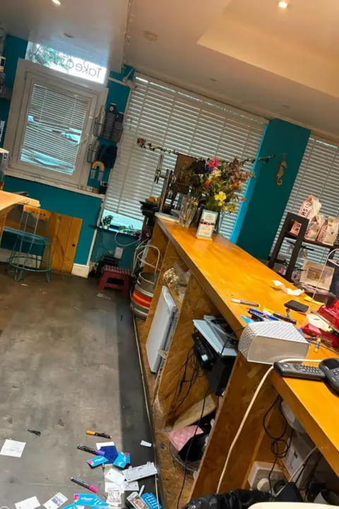 Sea Change Inside Sea Change cafe after the burglary. A window has been smashed and the blinds damaged. Objects, including paper and pens, have been thrown off the wooden counter and litter the floor.
