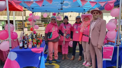 A group of people wearing pink clothes standing under a canopy for a charity fundraiser