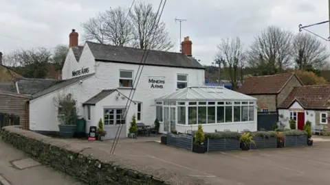 Google A white pub is pictured with a large conservatory at the front and a car park in front of that. The car park is empty. 