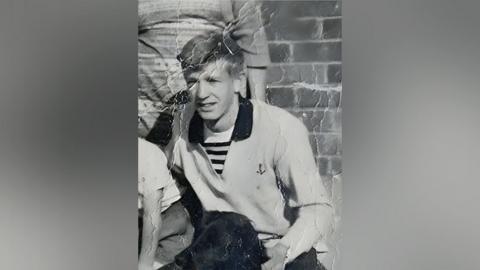 David Lawrence wearing a polo shirt in a black and white photo, sitting behind a dog