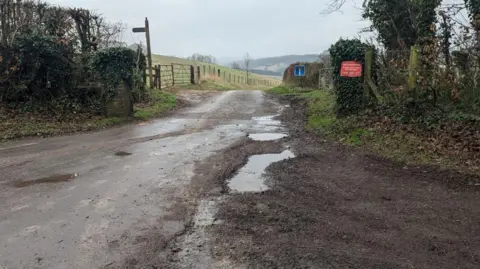 Numerous large puddle-filled potholes line a rural road in Wye, Kent. 